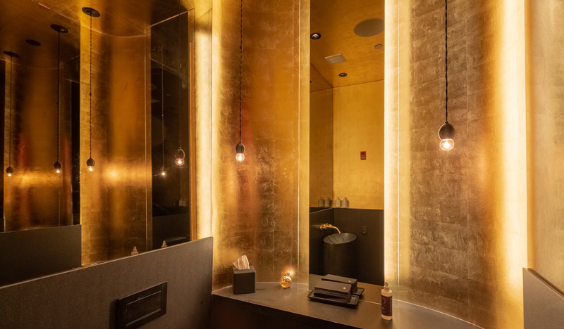 A mood-lit commercial bathroom with gold foiled wall decor